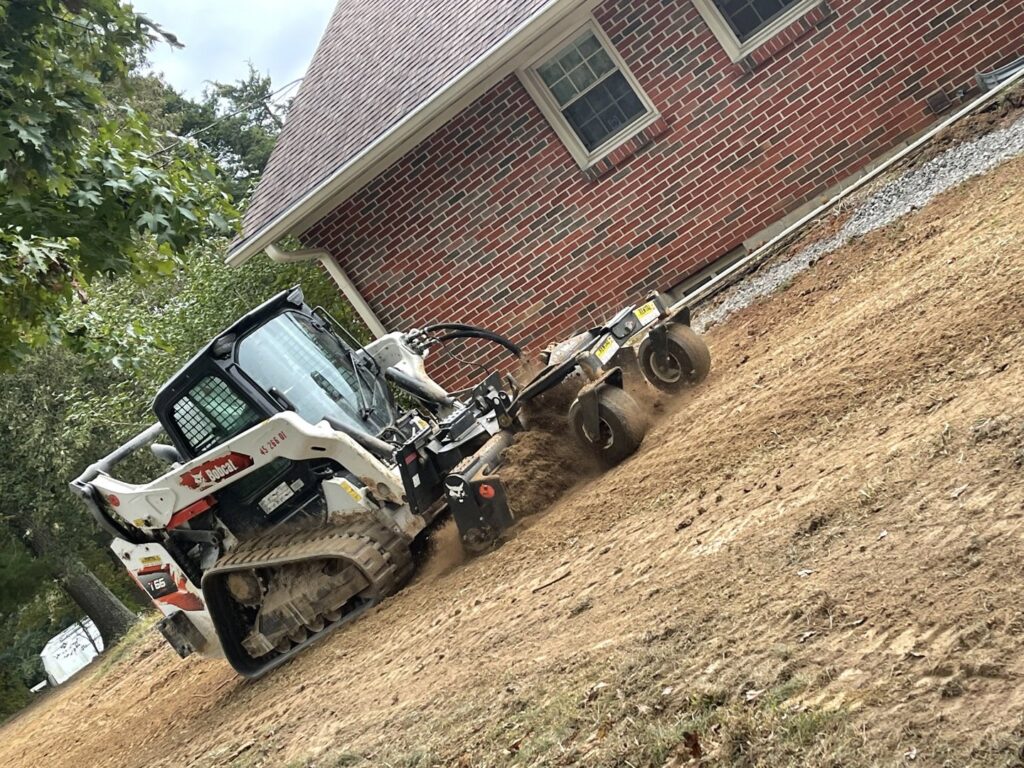 A Bobcat skid-steer loader performing excavation work on a sloped yard for drainage improvement by UpKeep Properties, LLC in Elizabethtown, KY.