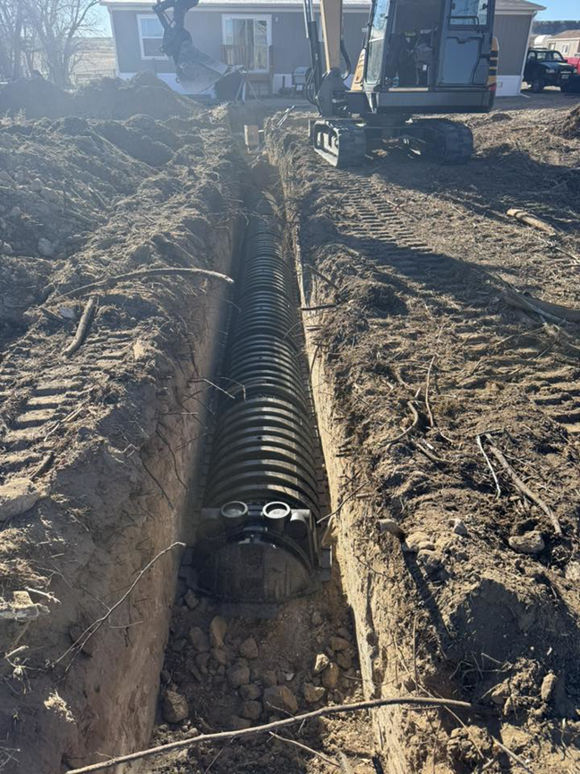 An excavator installing a large drainage system near a house for MP-X LLC Excavation and Construction in Riverton, WY