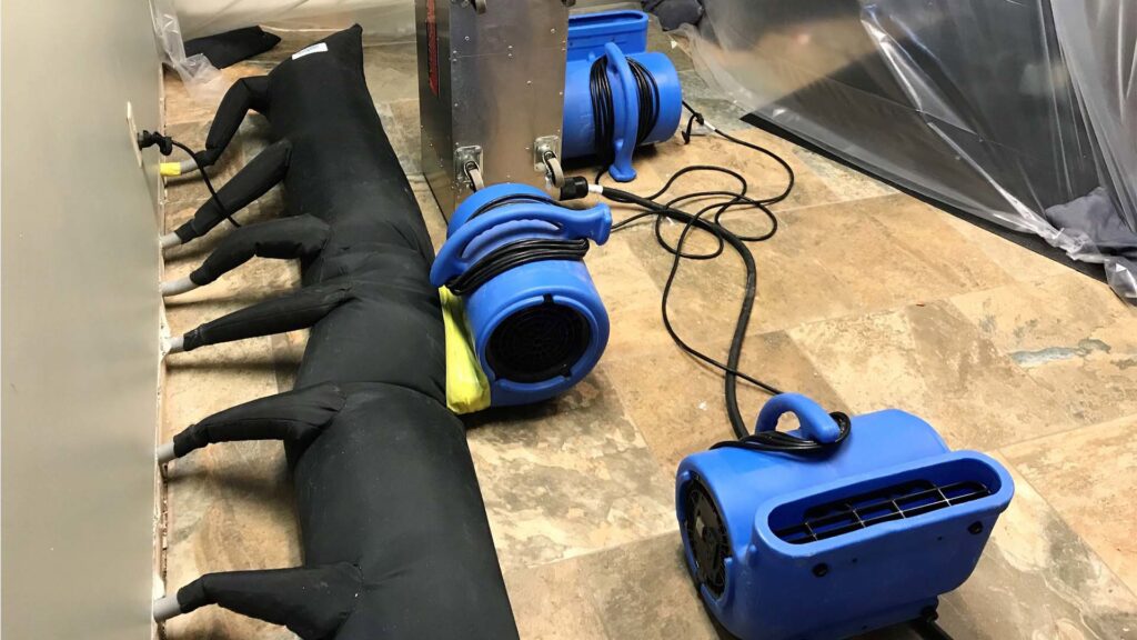 Specialized drying equipment, including blue air movers and a long black drying tube, used for water damage restoration by Absolute Water Mitigation & Restoration in Greeley, CO