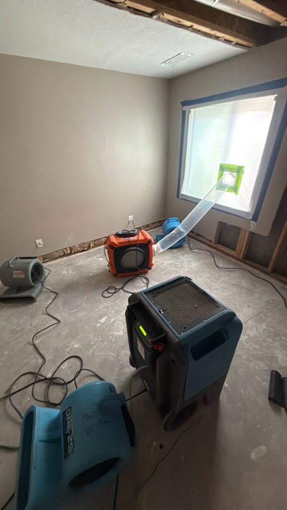 Multiple air movers and a dehumidifier set up in a room for drying after water damage in Syracuse, UT by Utah Disaster Specialists.