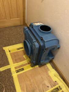 Professional drying equipment placed on a carpeted floor with caution tape during water damage restoration by Anytime Flood Restoration in Thornton, CO