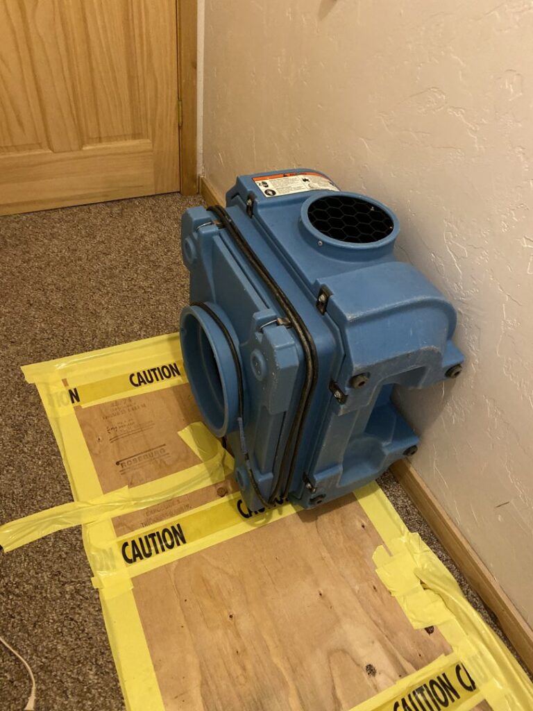 Professional drying equipment placed on a carpeted floor with caution tape during water damage restoration by Anytime Flood Restoration in Thornton, CO