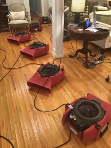 Air movers and drying equipment set up on a hardwood floor for water damage restoration by PuroClean of Tuscaloosa in Northport, AL.
