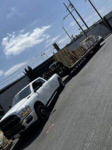 A white dually pickup truck towing a flatbed trailer loaded with wooden crates for Inglewood Transmission in Long Beach, CA.