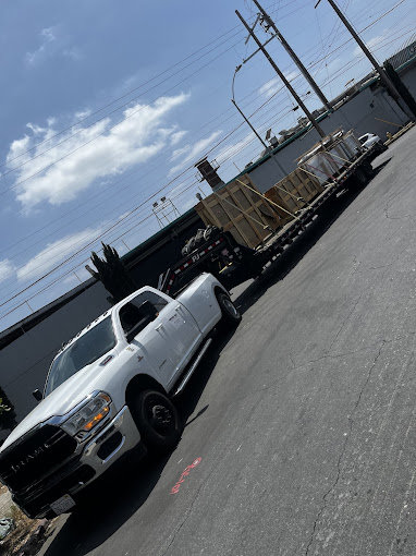 A white dually pickup truck towing a flatbed trailer loaded with wooden crates for Inglewood Transmission in Long Beach, CA.