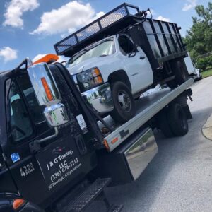 A white dump truck loaded onto a flatbed tow truck from J & G Towing, LLC, providing heavy vehicle transport in Greensboro, NC.