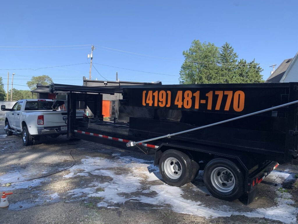 A large black dumpster trailer being washed, attached to a white pickup truck from Just Take It, LLC. in Yorba Linda, CA.