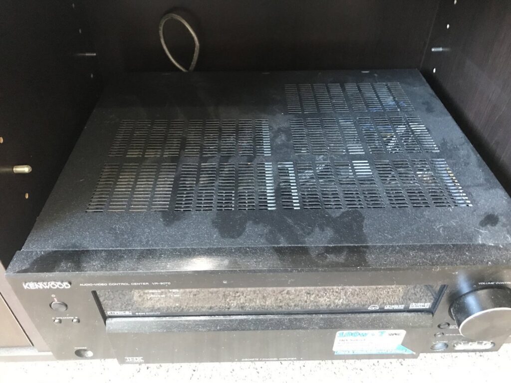 A dusty audio-video receiver on a shelf, showing accumulated dust before a professional cleaning by The Cleaning Fairy in Fort Lauderdale, FL.