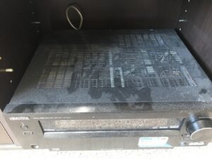 A dusty audio-video receiver on a shelf, showing accumulated dust before a professional cleaning by The Cleaning Fairy in Fort Lauderdale, FL.