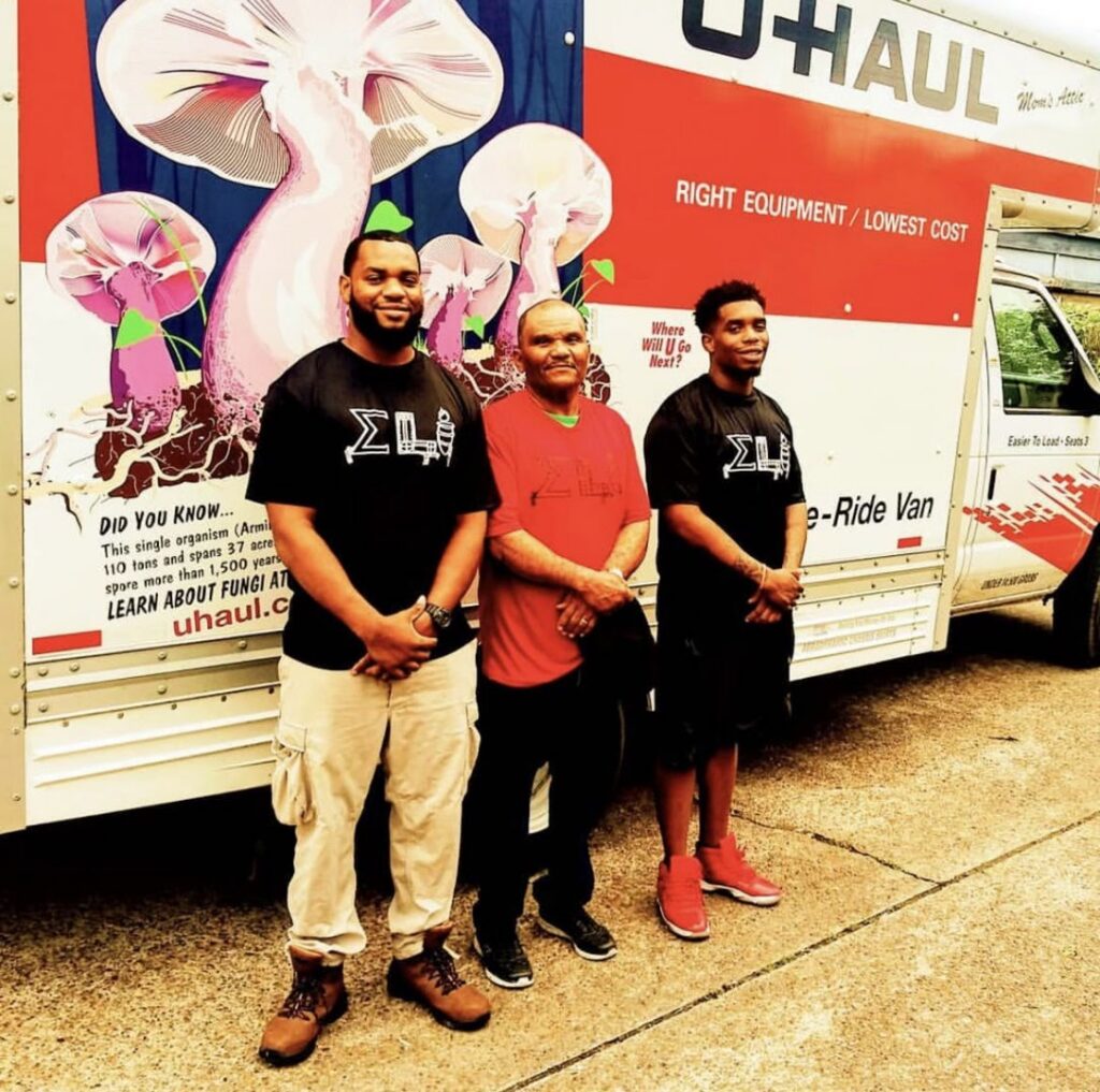 Three members of the E.L.I Movers LLC team standing proudly in front of a U-Haul moving truck in Houston, TX.