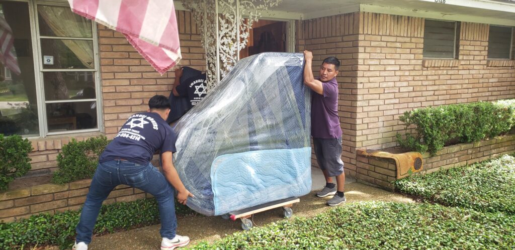 Emanuel Movers, Inc. team carefully moving a large, wrapped piano into a house in Houston, TX