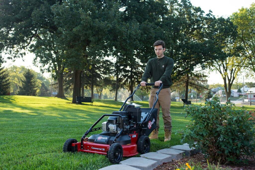 An employee of Nice & Precise Lawn Care expertly mowing a residential lawn with a commercial walk-behind mower in Ames, IA.