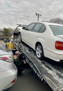 A Snoork Towing employee securing a white sedan onto a flatbed tow truck during a towing service in Charlotte, NC.
