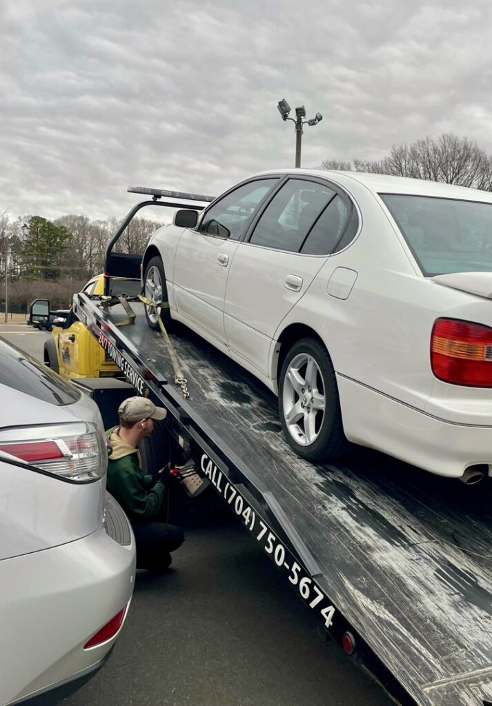 A Snoork Towing employee securing a white sedan onto a flatbed tow truck during a towing service in Charlotte, NC.
