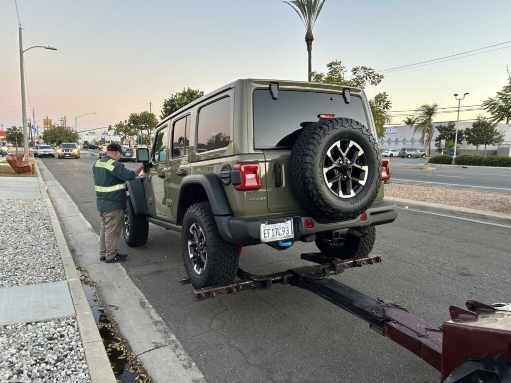 An Orellanas Towing & Junk Car employee preparing to tow a green Jeep Wrangler in Los Angeles, CA.