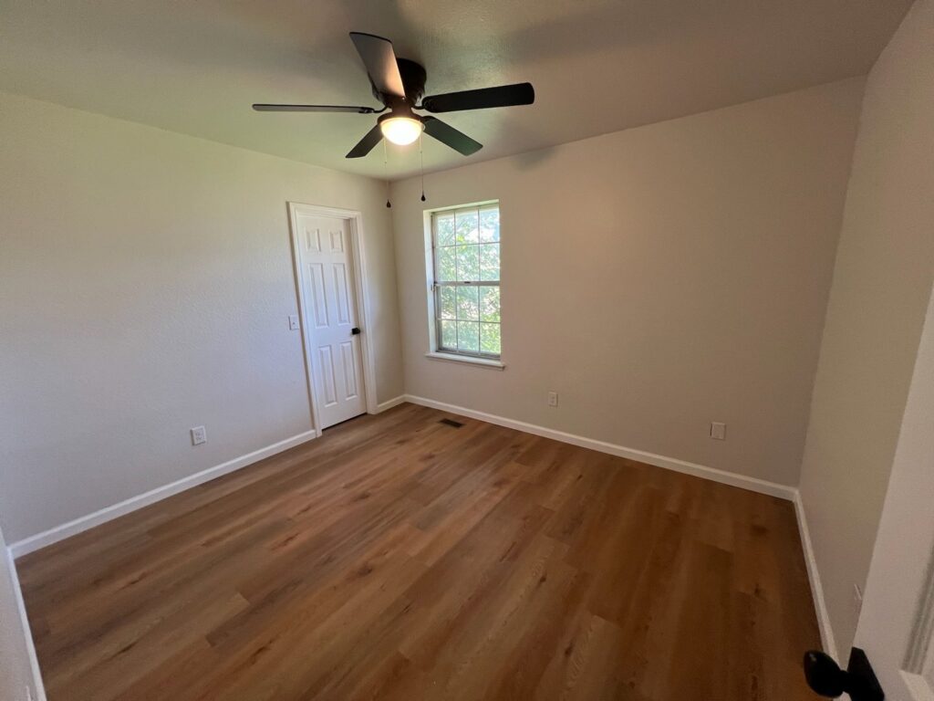A freshly cleaned, empty bedroom with wooden floors and a ceiling fan, showcasing Krys Cleaning's work in Oklahoma City, OK.
