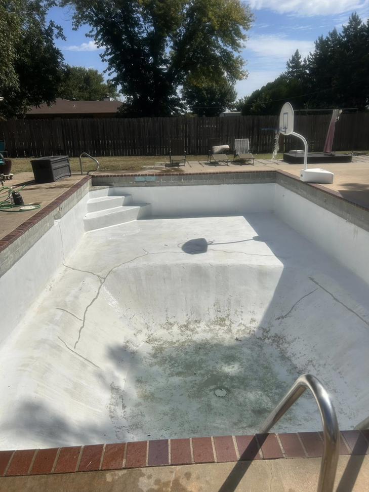 An empty in-ground pool showing cracks and residue, indicating a deep cleaning or repair job by Pips Pool Service in Enid, OK.