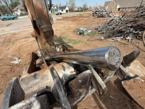 An excavator attachment holding a hydraulic cylinder with a debris pile in the background, by Enfield Demolition & Excavation LLC in Enid, OK.
