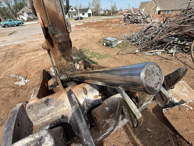 An excavator attachment holding a hydraulic cylinder with a debris pile in the background, by Enfield Demolition & Excavation LLC in Enid, OK.