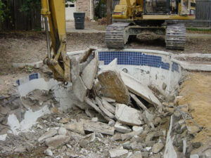 An excavator breaking up a concrete swimming pool during demolition by San Antonio Demolition Pros in San Antonio, TX.