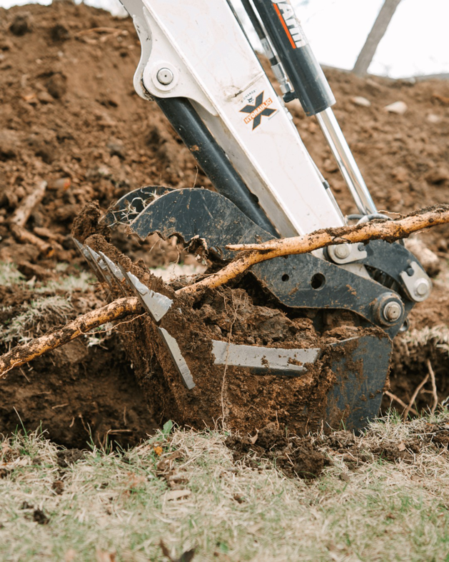 A close-up of an excavator bucket digging into the ground for plumbing work by Bright Side Plumbing in Overland Park, KS.