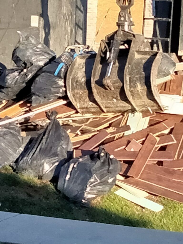 An excavator bucket positioned over a pile of demolition debris, including wood and trash bags, by HaysCo Facilities Management, Inc. in Dothan, AL.