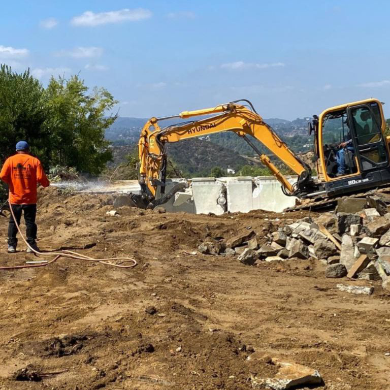 An excavator breaking up concrete on a demolition site with a worker from DEMO Leaders in Los Angeles, CA