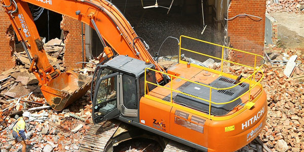 A large excavator demolishing a brick building, surrounded by rubble, by Youngstown Pro Demolition Services in Youngstown, OH.