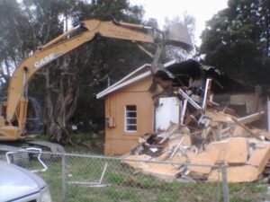 An excavator from Dade Wrecking Demolition LLC actively demolishing a residential house in Miami, FL.