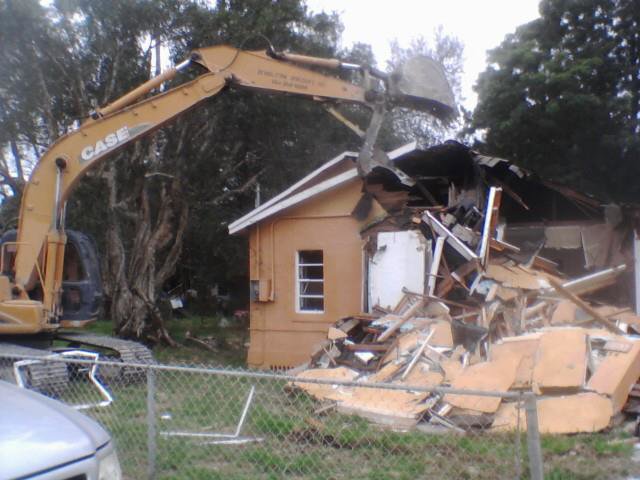 An excavator from Dade Wrecking Demolition LLC actively demolishing a residential house in Miami, FL.