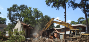 A wide shot of an excavator actively demolishing a residential house, showcasing Torrado Demolition's work in Houston, TX.