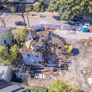 An excavator actively demolishing a residential building, showcasing demolition services by Rainstate Earthworks in Auburn, WA.