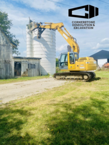 An excavator with a specialized attachment demolishing a large silo for Cornerstone Demolition & Excavation in Lexington, KY