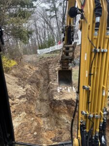 An excavator digging a trench for a drainage system at a job site for Fleury Dirt Works & Services Llc in Cumberland, RI