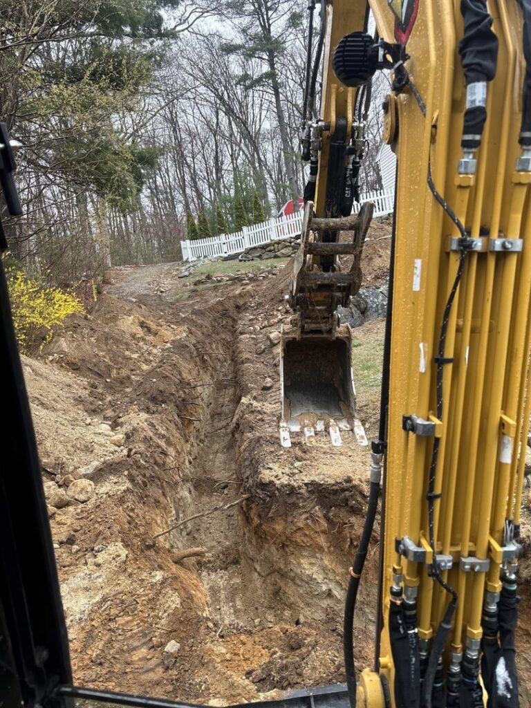 An excavator digging a trench for a drainage system at a job site for Fleury Dirt Works & Services Llc in Cumberland, RI