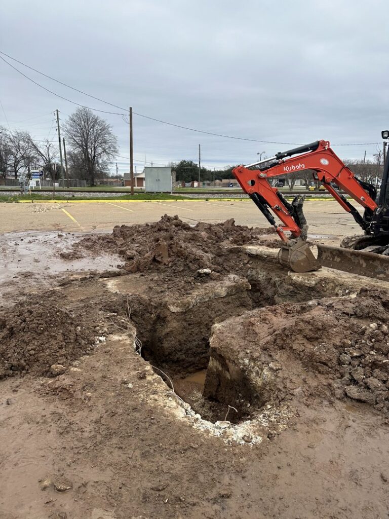 An excavator digging a large hole in a muddy site, indicating water damage repair by Robert Brown Plumbing, LLC in Bossier City, LA.
