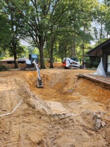 An excavator actively digging out a swimming pool for removal by East Shelby Demolition & Pool Removal in Olive Branch, MS.
