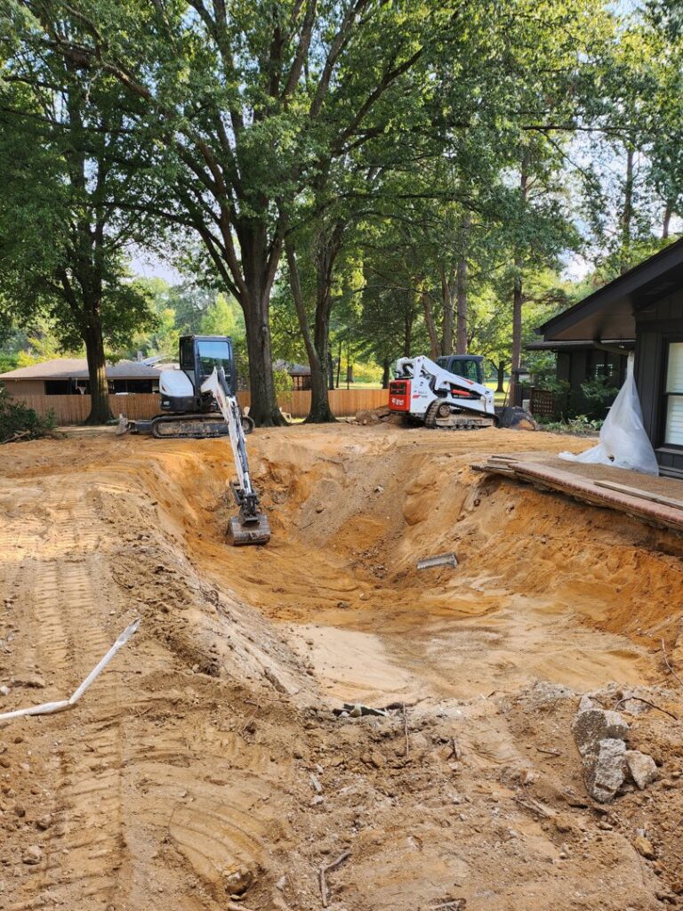 An excavator actively digging out a swimming pool for removal by East Shelby Demolition & Pool Removal in Olive Branch, MS.