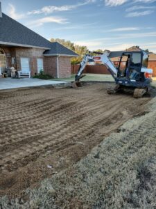 An excavator actively grading land next to a residential house by East Shelby Demolition & Pool Removal in Olive Branch, MS.