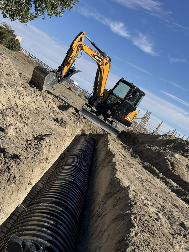 An excavator installing a large drainage pipe in a trench for MP-X LLC Excavation and Construction in Riverton, WY