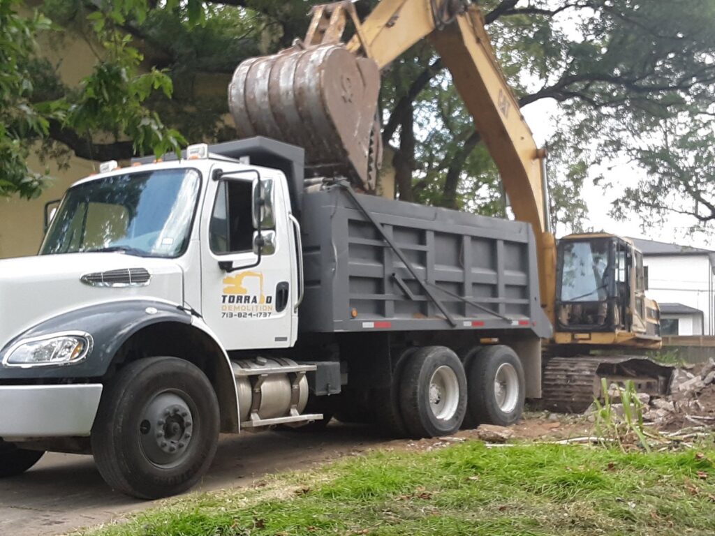 An excavator loading demolition debris into a dump truck on a job site, handled by Torrado Demolition in Houston, TX.