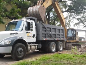An excavator loading demolition debris into a dump truck on a job site, handled by Torrado Demolition in Houston, TX.