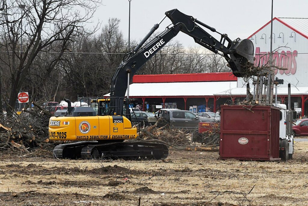 An excavator loading tree debris into a roll-off container, demonstrating site clearing services by Enfield Demolition & Excavation LLC in Enid, OK.