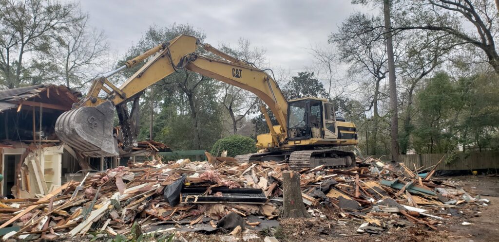 An excavator positioned on a large pile of demolition debris from a partially demolished house by Torrado Demolition in Houston, TX.