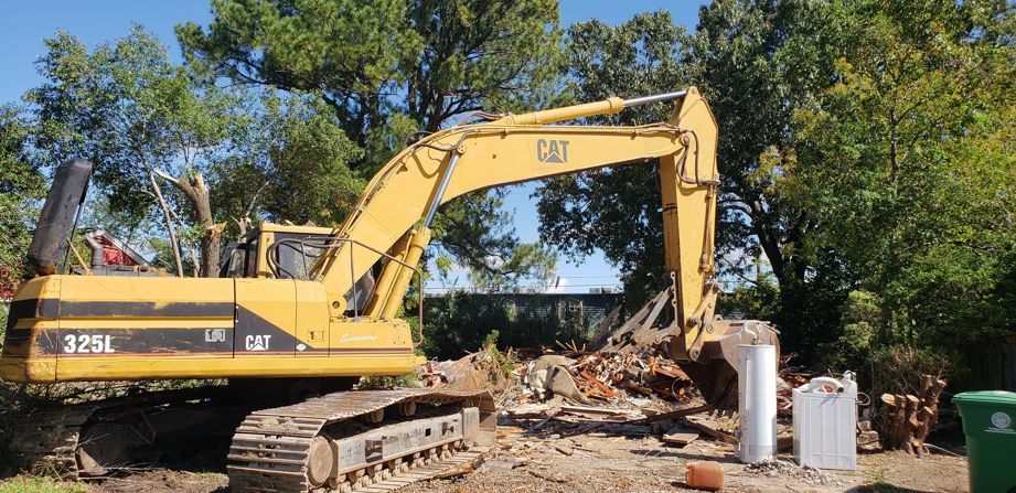 A large yellow excavator on a demolition site with debris, handled by Torrado Demolition in Houston, TX.