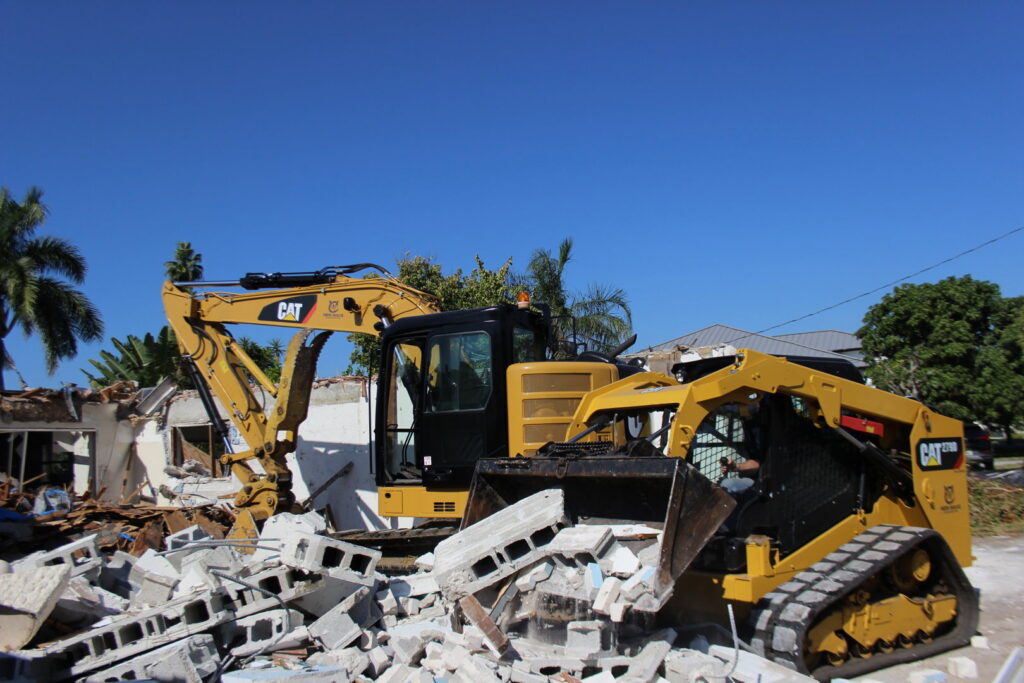 An excavator and skid steer actively demolishing a building and clearing debris for New Wave Concepts in Cape Coral, FL.