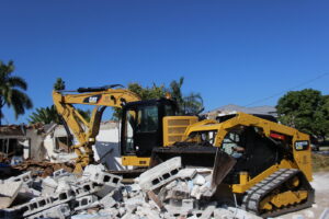 An excavator and skid steer actively demolishing a building and clearing debris for New Wave Concepts in Cape Coral, FL.