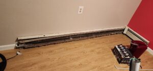 An exposed baseboard heating unit, possibly indicating a water leak or damage, being inspected by TCM Restoration & Cleaning in Anchorage, AK.