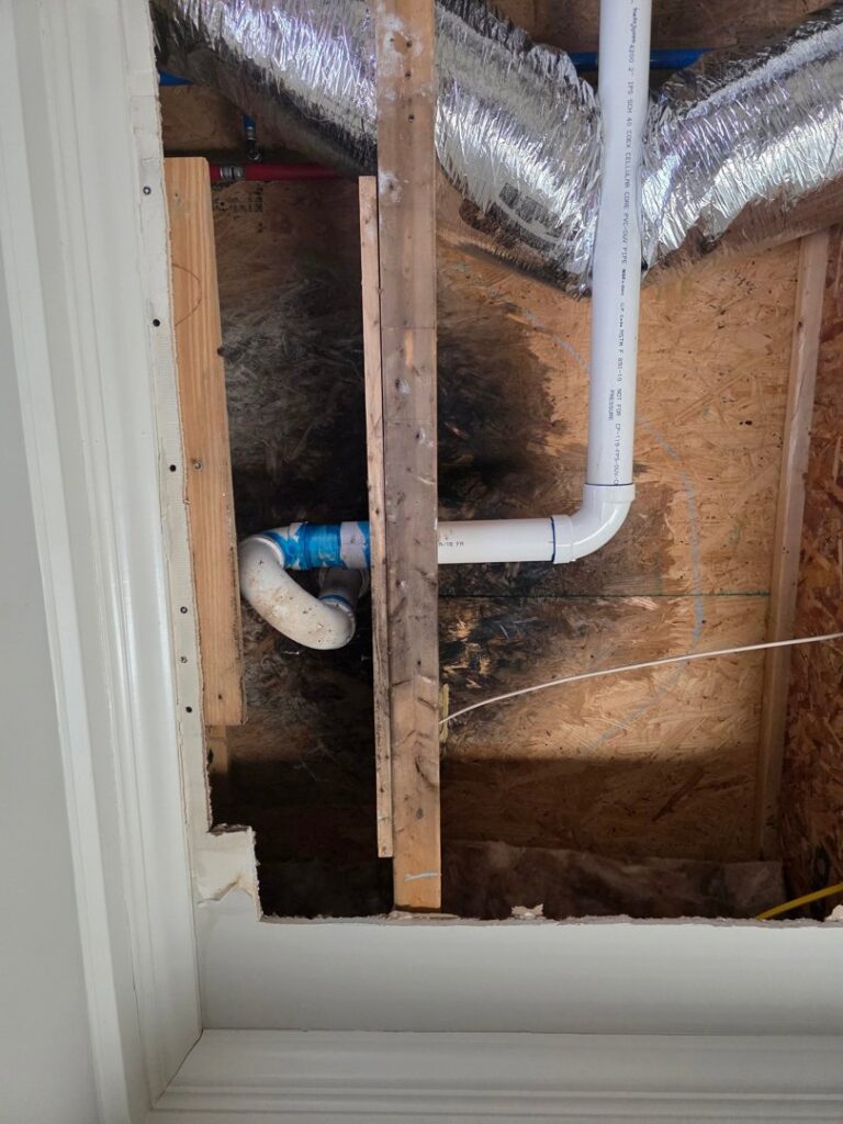 Exposed pipes and ductwork in a wall cavity with visible water stains on the wood, indicating hidden water damage by Restoration Specialist in O Fallon, MO.