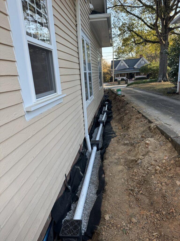An exterior foundation drainage system with pipes and gravel installed along a house by HNO Waterproofing & Slab Lifting Pros in Concord, NC.